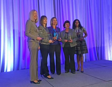 A group of women pose with trophys in front of a purple curtain