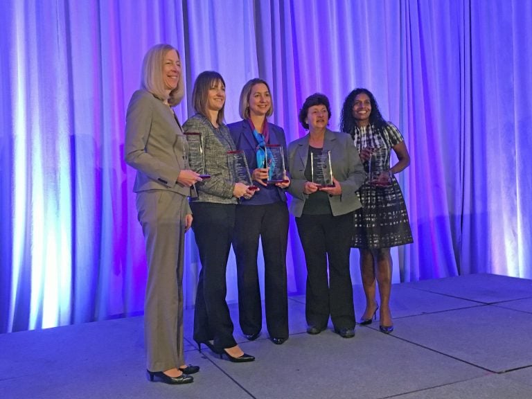 A group of women pose with trophys in front of a purple curtain