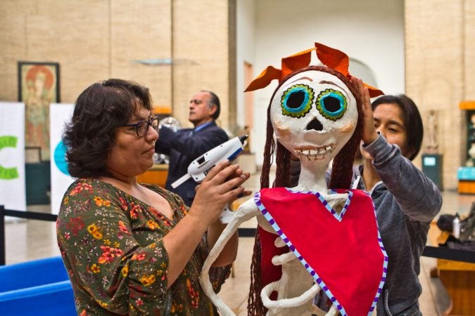 Artists Anna Palma (left) and Ivonne Pinto (right) work on the hair of a character for the Day of the Dead altar at the Penn Museum. (Kimberly Paynter/WHYY)