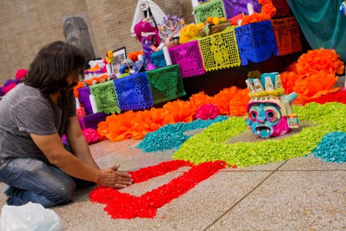 Artist Cesar Viveros arranges paper petals on the floor of the Day of the Dead altar. (Kimberly Paynter/WHYY)