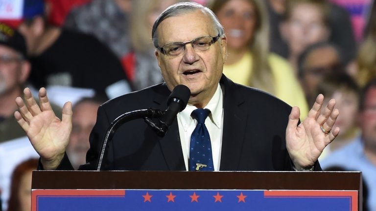 Man at a podium, hands up, palms towards the camera; crowd of people blurred in the background