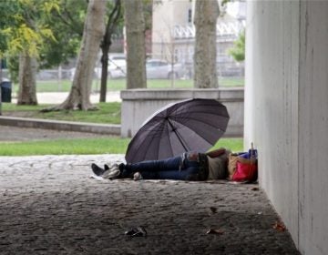 A homeless person is shown sleeping under an umbrella.