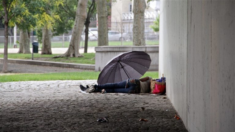 A homeless person is shown sleeping under an umbrella.