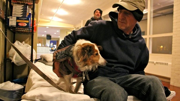 A man sits on a cot, his dog at his side