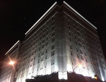 Bright lights illuminate an imposing grey stone building against a dark night sky