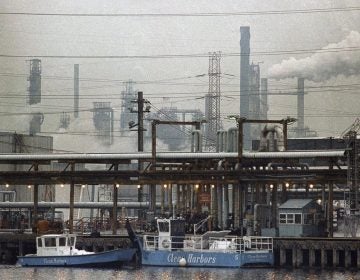 two clean harbor cleanup boats work in a waterway alongside an industrial refinery, smoke stacks in the background