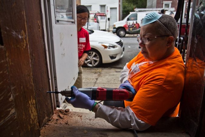 A woman uses a hand drill as another woman looks on