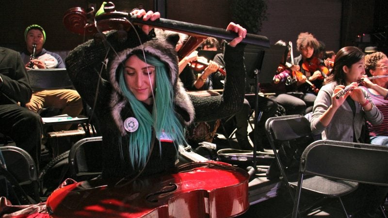 Bexx Rosenbloom, a former Philadelphia middle school teacher, plays her broken cello as a percussion instrument during a rehearsal at the 23rd Street Armory. (Emma Lee/WHYY)