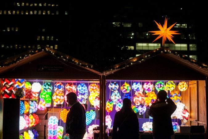 Shoppers stand in front of a shop selling oversized Christmas tree ornaments at the LOVE Park Christmas Village Friday. (Brad Larrison for WHYY)