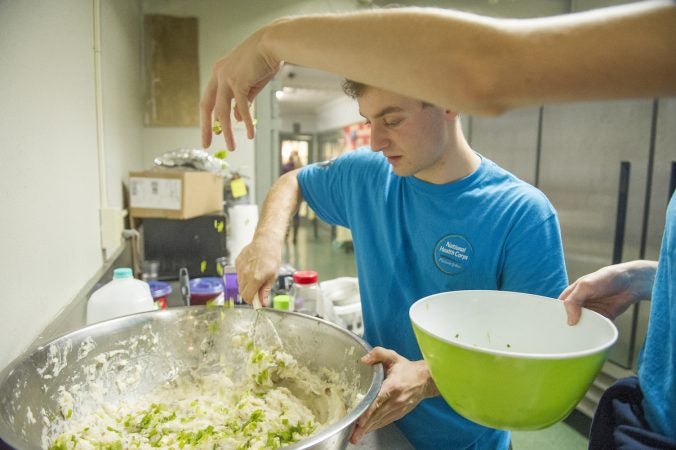 Volunteer Issac Dayno mixes mash potatoes while volunteer Jessica Hughes adds scallions. (Jonathan Wilson for WHYY)