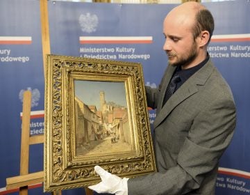 A museum worker carries a 19th century painting by Polish artist Robert Sliwinski during a ceremony Wednesday in Warsaw, Poland. The work was looted by the Nazis during World War II and recently recovered in the U.S. by the FBI. (Alik Keplicz/AP)