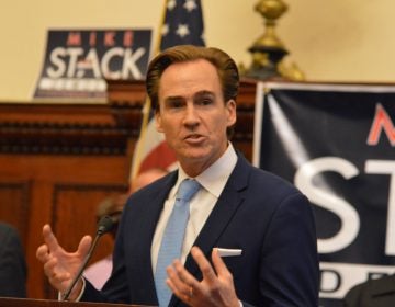 A man speaks with campaign signs visible behind him.