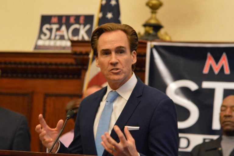 A man speaks with campaign signs visible behind him.