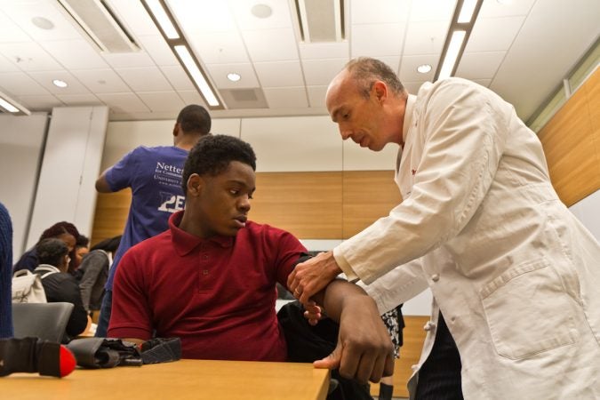 Trauma surgeon Jeremy Cannon, M.D., demonstrates how to put a tourniquet on Sayre 11th grade student, Jahaad Olaore. (Kimberly Paynter/WHYY)