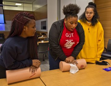 Charlie White (center), 12th grade student at Sayre, practices applying compression to a wound on a mannequin, while Danny Miles (right) and Kayla Fryer (left), look on. (Kimberly Paynter/WHYY)