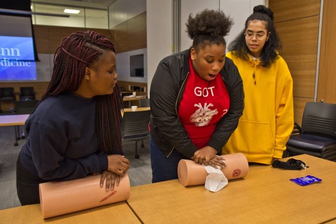 Charlie White (center), 12th grade student at Sayre, practices applying compression to a wound on a mannequin, while Danny Miles (right) and Kayla Fryer (left), look on. (Kimberly Paynter/WHYY)