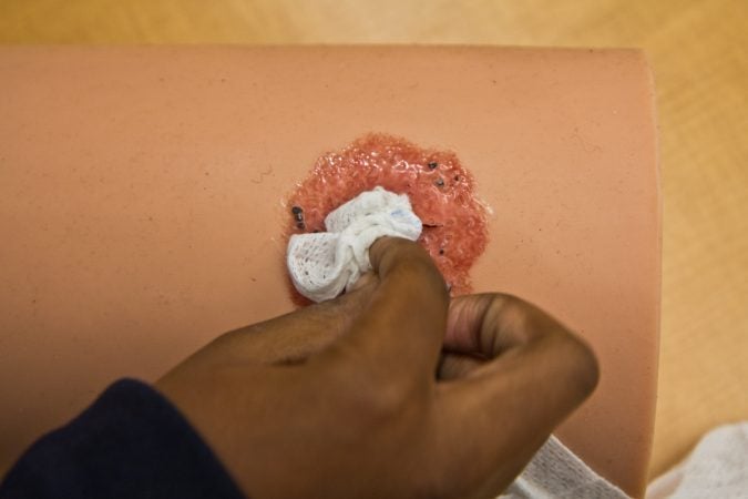 A student practices packing a “shotgun” wound on a mannequin at a Stop The Bleed training. (Kimberly Paynter/WHYY)