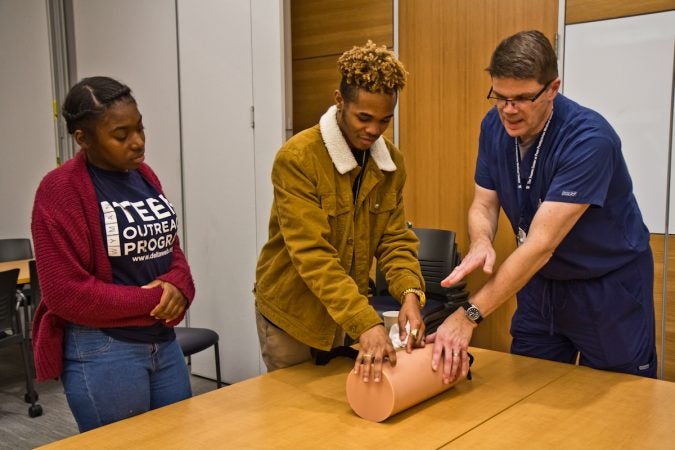 Najeer Francis, an 11th grade student at Sayre, practices packing a wound on a mannequin under the supervision of John Gallagher, trauma program coordinator. (Kimberly Paynter/WHYY)