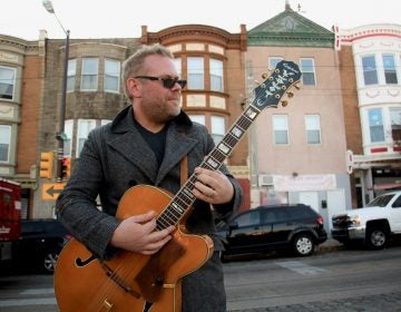 Colton Weatherston plays his guitar in front of colorful building facades on Germantown Avenue