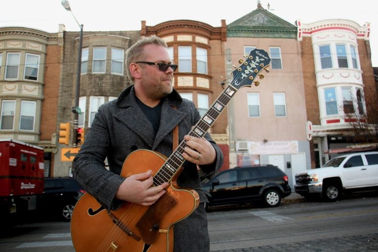 Colton Weatherston plays his guitar in front of colorful building facades on Germantown Avenue