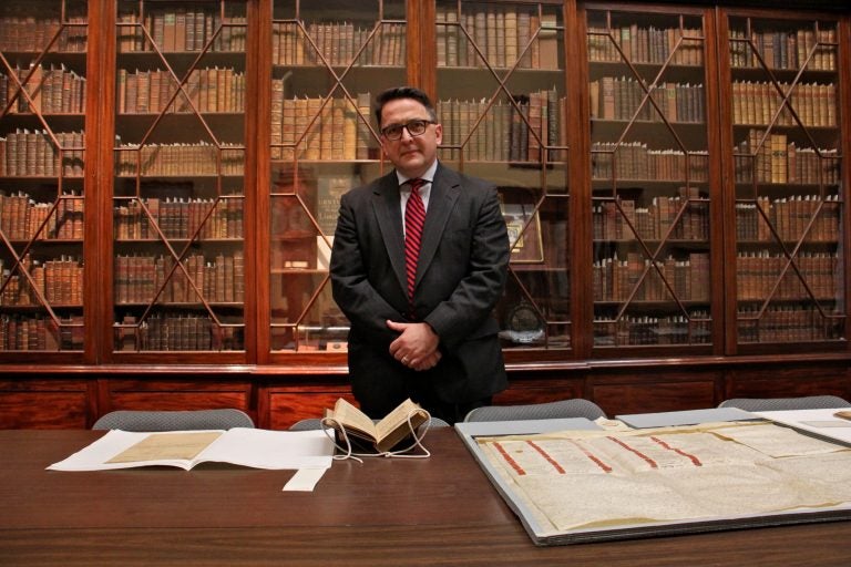 Michael Barsanti, director of the Library Company of Philadelphia, stands before a glass fronted bookcase