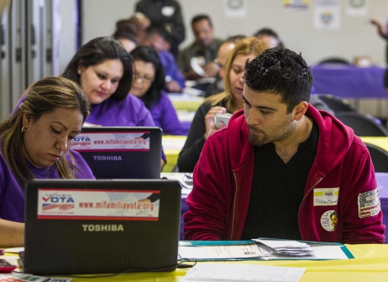 FILE - In this Monday, March 31, 2014 file photo, SEIU-UHW worker Kathy Santana, left, assists Ruben Torres, 27, during a health care enrollment event at the SEIU-UHW office in Commerce, Calif.