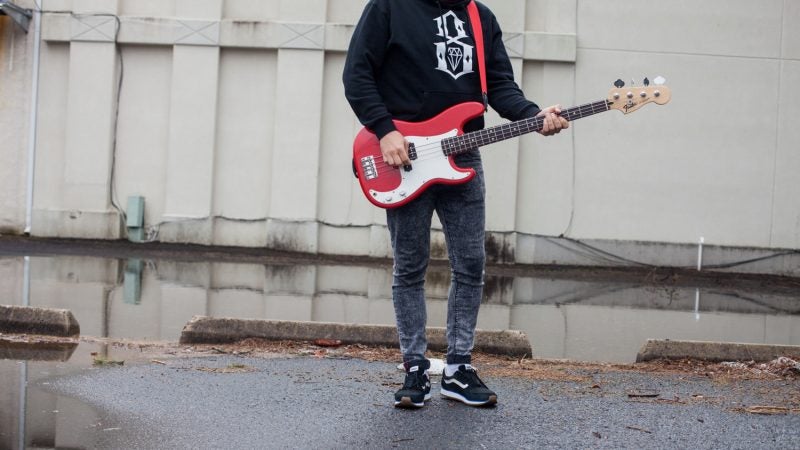 Viktor, an undocumented immigrant from Belarus seeking asylum in the U.S, strums a bass guitar. He left Belarus with a bandmate and hopes to play music again if he is able to attain legal status. (Brad Larrison for NewsWorks)