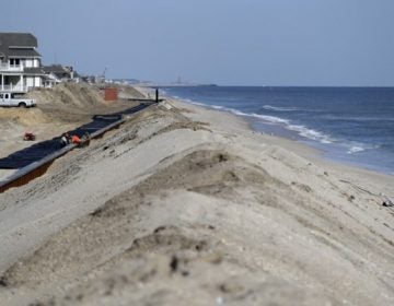 A woman, right, scavenges on the beach while workers labor on the new seawall construction project to protect Mantoloking, New Jersey, from the Atlantic Ocean. As the third anniversary of Superstorm Sandy approaches, New Jersey says it has acquired 90 percent of the easements it needs to do shore protection work along the coast. New Jersey is beginning to exercise its power of eminent domain to secure other easements. (AP file photo)