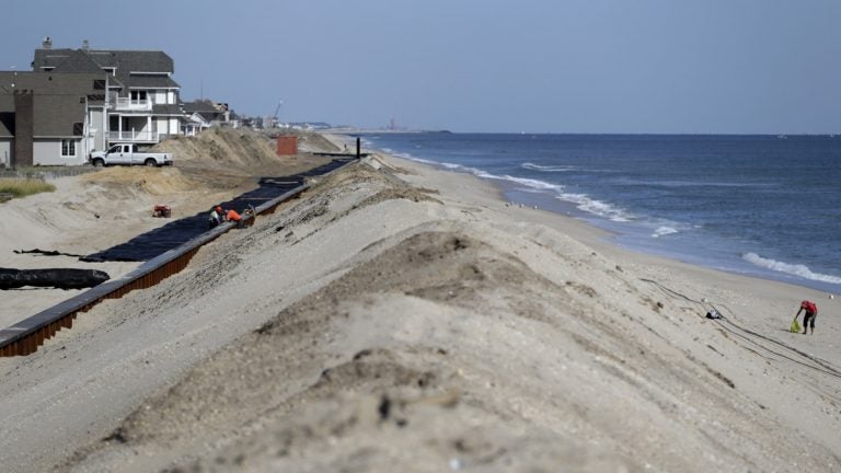 A woman, right, scavenges on the beach while workers labor on the new seawall construction project to protect Mantoloking, New Jersey, from the Atlantic Ocean. As the third anniversary of Superstorm Sandy approaches, New Jersey says it has acquired 90 percent of the easements it needs to do shore protection work along the coast. New Jersey is beginning to exercise its power of eminent domain to secure other easements. (AP file photo)