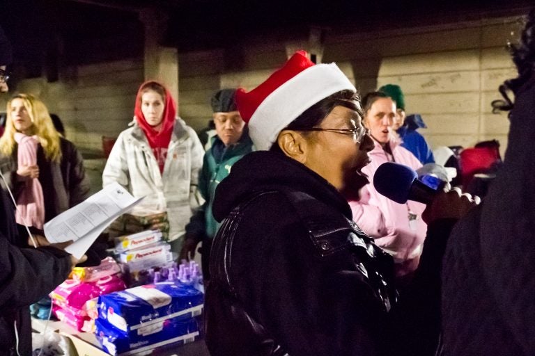 Asteria Vives, head of Home Quarters and Friends, sings carols at the Emerald Street and Lehigh underpass, in the Kensington section of Philadelphia. (Kimberly Paynter/WHYY)