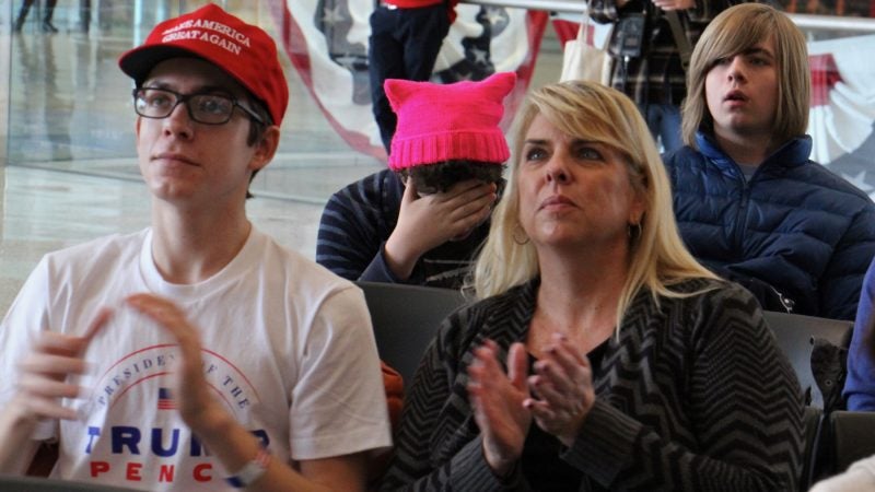 Thomas Dintino, 16, (left) and his mother Karen, from Marlton, New Jersey, applaud as Donald Trump is sworn in as president while Dashiell Ward, 15, of Philadelphia, looks away. About 50 people watched the inauguration on the big screen at the National Constitution Center. (Emma Lee/WHYY)