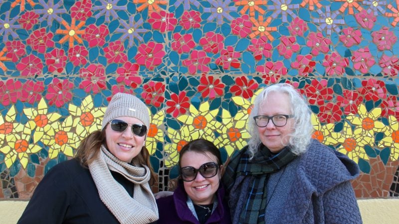 Standing in front of one of the McClure School murals (from left) Principal Shanon Marino, art teacher Becky Naughton, and teaching artist Kimberly Niemela look forward to completing the project this year.
