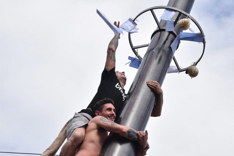 Competitors in the greased pole challenge at the Italian Market Festival reach the prizes at the top.