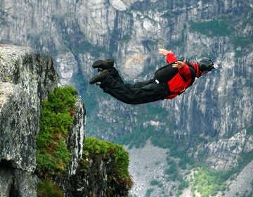 Man jumping off a cliff with a parachute