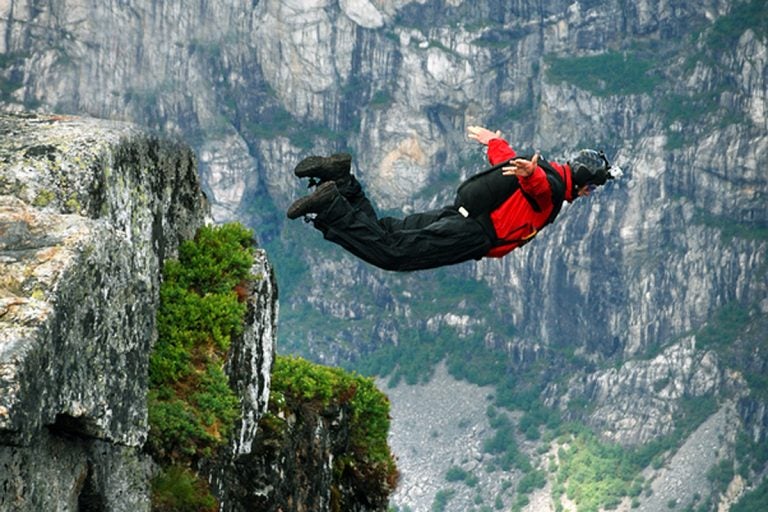 Man jumping off a cliff with a parachute