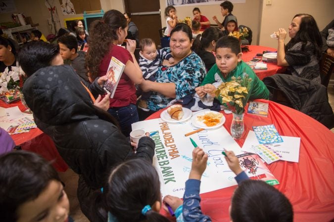 Marlene Arabs, center, holds her friends baby, Brian Orellana, as they mingle with friends and family at APM's Three Kings Day/Octavious celebration for diplaced families from Puerto Rico in North Philadelphia on January 12 2018. (Emily Cohen for WHYY)