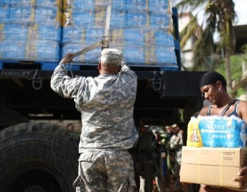 A U.S. Army soldier unloads a shipment of water provided by FEMA as a resident walks past in San Isidro, Puerto Rico