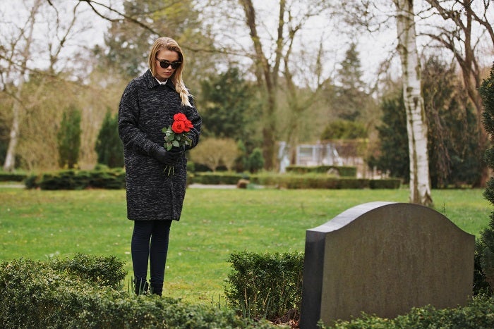 Young woman visiting a loved one at the cemetery paying respects with fresh rose flowers. Female grieving at graveyard.