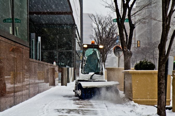 A Bobcat driver with a front brush works to keep the sidewalks around the Federal Reserve clear. (Kimberly Paynter/WHYY)