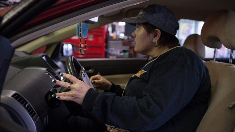 Sue Sweeney, 41, the shop forewoman for Girls Auto Shop, shows off her Eagles manicure as she checks lights on a car that has come into the shop. (Emily Cohen for WHYY)