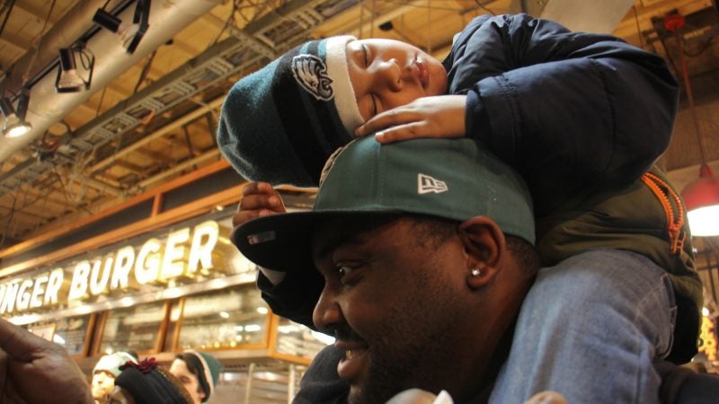 Young Eagles fan Howard McKelvey IV falls asleep on his father's shoulders during an Eagles event at Reading Terminal Market. (Emma Lee/WHYY)