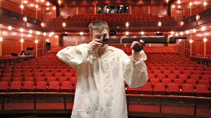 Penn Charter student Etthan Willis raises a prop gun on stage at the David L. Kurtz Center for the Performing Arts before a performance of 