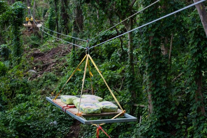 A cargo sled descends the zip line, carrying bags of concrete to a work crew below.