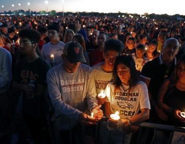 Jorge Zapata, Jr., center, a student at Marjory Stoneman Douglas High School, holds candles with his mother Lavinia Zapata, and father Jorge Zapata, Sr., during a candlelight vigil for the victims of the Wednesday shooting at the school, in Parkland, Fla., Thursd