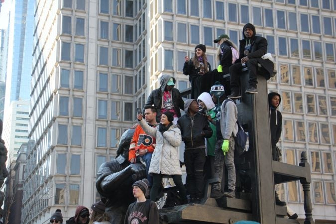Eagles fans perch on a statue in Thomas Paine Plaza, watching the Super Bowl celebration on a jumbotron. (Emma Lee/WHYY)