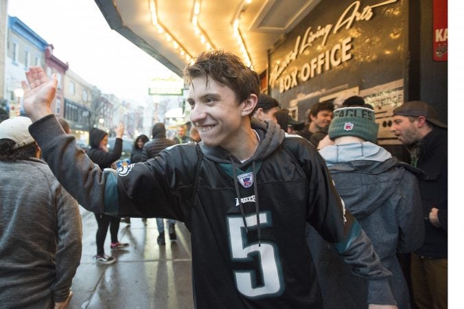 A senior from Strath Haven High School in Wallingford high fives Eagles fans as the pass by in from of the TLA on South St.