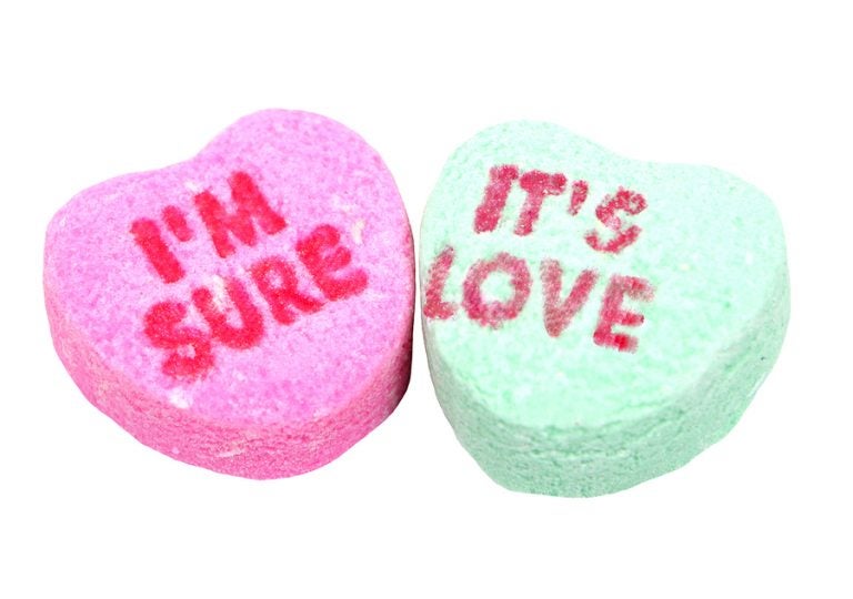 two candy hearts traditionally given around valentine's day with the message i'm sure it's love
