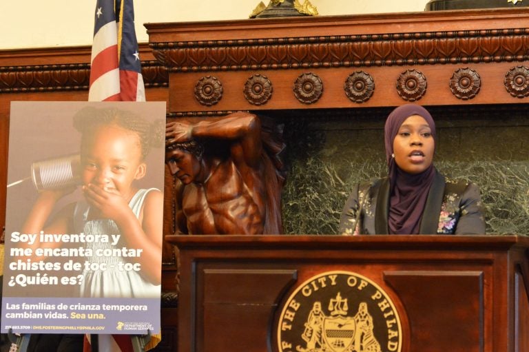 Stephanie Laws talks about the joys of being a foster parent, flanked by a sign with information about a new campaign to recruit more of them. (Tom MacDonald/WHYY)