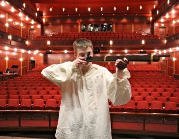 Penn Charter student Etthan Willis raises a prop gun on stage at the David L. Kurtz Center for the Performing Arts before a performance of 