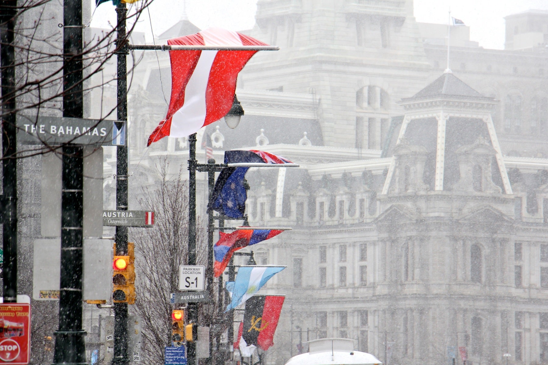 The flags of many nations that line the Ben Franklin Parkway are battered by strong winds as snow falls in Center City.